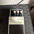 Bílý efekt pedál s černým spínacím tlačítkem. Na zařízení jsou nápisy BOSS, Noise Suppressor NS-2 a popisky ovládacích prvků REDUCTION, MODE, OUTPUT,…