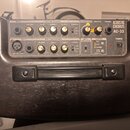 Kytarový zesilovač v tmavém dřevění provedení s ovládacím panelem. Na panelu jsou nápisy ACOUSTIC CHORUS AC-33, GUITAR CHANNEL a MIC/LINE CHANNEL. Js…