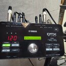 Černý modul elektronických bubnů s nápisy YAMAHA a DTX drums. Displej zobrazuje červené číslo 120 a zelený text KIT1 01:Maple Custom. Na spodní pravé…