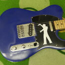 Modrá elektrická kytara typu Telecaster s černým pickguardem. Na pickguardu je bílá silueta postavy v pohybu. Hриф je vyroben ze světlého dřeva, kyta…