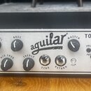 Stříbrný basový zesilovač s černým horním krytem. Na předním panelu je nápis TONE HAMMER 500 a logo aguilar. Panel obsahuje ovládací knoflíky s popis…