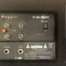 Zadní panel kytarového komba s černým povrchem. V horní části je nápis „M.a.g.g.i.e.“ a logo „Mc CRYPT“. Panel obsahuje čtyři otočné potenciometry s…