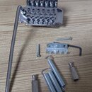 Krom chromovaného tremolo mostu s pákou jsou na fotce vidět tři pružiny, dva cylindrické díly a kovový držák s dvěma šrouby a imbusovým klíčem. Na mo…