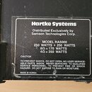Detailní záběr na zadní část černého zařízení s nalepeným informačním štítkem. Na štítku je uveden nápis Hartke Systems, Distributed Exclusively by S…