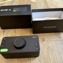 Černý audio rozhraní s nápisem evo 4. Přístroj má uprostřed velký ovládací knoflík, několik tlačítek s označením 48V, 1, 2 a ikonami mikrofonu a hlad…