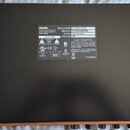 Fotografie zachycuje spodní stranu černého rackového zařízení. Uprostřed je nalepený bílý štítek s texty: PRODUCT NAME ELEVEN RACK, SERIAL NO DFDKB34…