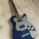 Tmavě modrá elektrická kytara s kovovým pickguardem a hnědým hmatníkem. Nástroj má dva humbuckery, tři ovládací knofíky a jeden přepínač. Na hlavě kr…