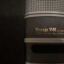 Detail kondenzátorového mikrofonu s černým povrchem a stříbrnou mřížkou. Na těle je zlatý nápis Vintage V 67, pod ním číslo 23-2334 a text JZ Microph…