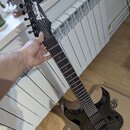 Černá elektrická kytara s tmavým hnedým hmatníkem a černým hardwarem. Na hlavě je bílý nápis Ibanez. Tělo kytary má lesklý povrch a je vybavena dvěma…