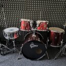 Vícedílná bicí souprava v tmavě červené barvě s chromovaným kováním. Na basovém bubnu je bílé logo Gretsch, stejné logo je viditelné i na ostatních b…