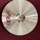 Kruhový činel stříbrné barvy s viditelným koncentrickým rýhováním povrchu. Na levé straně je svisle umístěné červené logo PAiste a pod ním menší nápi…