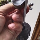 Detailní záběr na horní část chromovaného stojanu s černým plastovým utahovacím knoflíkem. Na stojanu je připevněn kovový držák s imbusovým šroubem.…