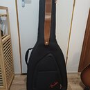 Černý polotvrdý obal na kytaru s hnědým koženým pruhem v horní části. V dolní části je červené logo Fender. Obal vypadá být v dobrém stavu.