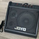Černý kytarový kombo zesilovač s kovovou mřížkou včelíkového vzoru. Na přední straně je umístěno bílé logo JOYO. Horní panel obsahuje červený vypínač…