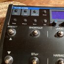 Černý efektový pedál s nápisem TC HELICON. Horní panel obsahuje tlačítka Tone, Pitch (Hold to Edit), Guitar FX a Home, dále Setup, Wizard, Store a Ed…