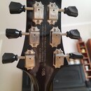 Zadní strana černé hlavy elektrické kytary s šesti stříbrnými ladičkami a černými knoflíky. Uprostřed je bílý nápis: Built by Cor-Tek Musical Instrum…