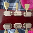 Zadní strana tmavě červené hlavy kytary s šesti ladicími mechanismy krémové barvy. Na kovových krytech ladíček jsou nápisy GIBSON DELUXE. V levé část…