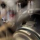 Fotografie zachycuje vnitřek kytarového komba s viditelnými elektronkami a reproduktorem. Na jedné z elektronek je červený nápis EL34 a logo s písmen…