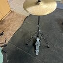 Zlatý kovový činel umístěný na černém kovovém stojanu. Na spodní části stojanu je viditelný stříbrný pedal s nápisem Tama. Povrch činelu vykazuje běž…