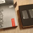 Fotografie zobrazuje sadu snímačů v originálním balení. Na krabici jsou nápisy PICKUPS, GUITAR a logo EMG; na štítku je uvedeno EMG PICKUPS FOR GUITA…