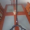 Černý kovový stojan s trojnožkou a horní vodorovnou opěrkou potaženou černým materiálem. Stojan je umístěn na dřevěném stole s prosklenou deskou. Na…