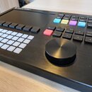 Černý elektronický sekvencer Polyend Tracker s displejem a mřížkou bílých tlačítek. Na horní hraně je nápis Polyend Tracker. Zařízení obsahuje barevn…