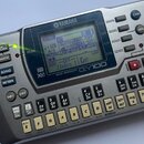 Šedý digitální sekvencer s displejem a množstvím tlačítek. Na horní straně je logo YAMAHA a pod displejem nápisy GENERAL MIDI XG, MUSIC SEQUENCER a Q…