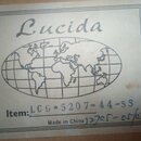 Fotografie zachicuje bílou papírovou nálepku s černým tiskem. Je na ní vidět nápis Lucida, grafický symbol zeměkoule a text Item: LCG-5207-44-SS. Dol…