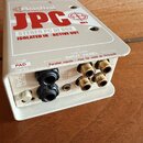 Bílá DI box s nápisem Radial JPC MK3 STEREO PC DI BOX ISOLATED IN - ACTIVE OUT. Na předním panelu jsou dva vstupní konektory jack, čtyři výstupní kon…