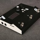 Černý elektronický přístroj s bílým bočním panelem. Na horní straně se nachází displej, bílý otočný knoflík a několik tlačítek s kovovými hlavicemi.…