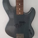 Tělo elektrické kytary v matné šedé barvě s hnedým hmatníkem z dřeva a bílými tečkovými značkami. Nástroj nemápickguard ani ladicí kolíky, v místě sn…