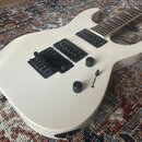 Bílá elektrická kytara s dvěma černými humbuckery a černým mostem. Na těle jsou dva černé otočné knoflíky a jeden přepínač. Povrch nástroje je hladký…