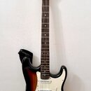 Elektrická kytara s tłem v provedení sunburst a bílým pickguardem. Na hlavě hředu je viditelné logo "Squier". Nástroj má tři snímače typu single-coil…