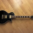 Černá elektrická kytara s tvarem singlecut a bílým lemováním. Na hlavě je viditelné logo Epiphone. Nástroj má dva humbuckery, zlatý hardware a hриф s…
