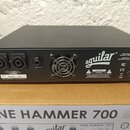 Černý basový zesilovač značky aguilar. Na zadní straně jsou dva výstupy pro reproduktory, tuner output a ventilátor s kovovou mřížkou. Na štítku je u…