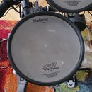 Elektronický buben s bílým nylonovým povrchem. Na horní části je nápis Roland a v dolní části logo V-Drums spolu s textem o patentech. Nástroj je sou…