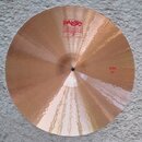 Kruhové činely z bronzu s viditelným broušením povrchu. Na horní části je červené logo Paiste 2002 s nápisy TRADE MARK a MADE IN SWITZERLAND. V pravé…