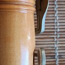 Detail dřevěného dechového nástroje v přirozené světle hnědé barvě. Na instrumentu jsou vidět dvě kovové klapky, jedna z nich má na konci plstěnou po…
