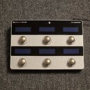 Stříbrný MIDI kontrolér s nápisy SINGULAR SOUND a MIDI MAESTRO. Zařízení má dvě řady tří modrých displejů a dvě řady tří kulatých kovových tlačítek.…