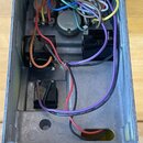 Fotografie zachycuje vnitřek šedého kovového šasi elektronického zařízení. Uvnitř jsou vidět zapojená deska plošných spojů, transformátory a svazek b…