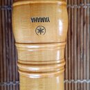 Detail dřevěného nástroje v přirozené světle hnědé barvy. Na povrchu je černý nápis YAMAHA a pod ním logo značky Yamaha v kroužku. Povrch je hladký a…