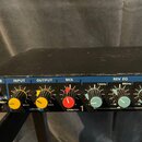 Černý rackový efekt s ovládacími prvky na předním panelu. Jsou zde nápisy REVERB, INPUT, OUTPUT, MIX a REV EQ s pripadujícími knoflíky. U ovládání MI…
