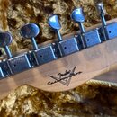 Zadní strana hlavy kytary z přírodního dřeva s chromovanými ladičkami. Na dřevě je černý nápis Fender Custom Shop. Povrch dřeva vykazuje drobné škráb…