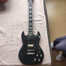 Černá elektrická kytara s dvojstupňovitým tělem a hnědým hmatníkem. Nástroj má dva humbuckery, čtyři ovládací knoflíky a stрійkový most. Na hlavě kyt…