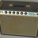 Kytarový zesilovač v černém krytu s kovovou rukojetí. Na ovládacím panelu jsou nápisy INSTRUMENTS, VOLUME, TREBLE, BASS, REVERB, SPEED a INTENSITY, v…