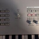 Detailní záběr na ovládací panel stříbrného syntezátoru s klávesami. Panel obsahuje několik sad tlačítek, otočný knoflík SPEED a sekci ARPEGGIATOR s…
