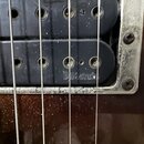 Detailní záběr na dvě černé snímače s viditelnými póly, které jsou osazeny v kovovém rámečku. Na spodním snímači je vyražen nápis DiMarzio. Povrch ko…