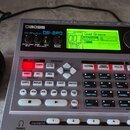 Šedý elektronický doprovodný automat Boss Dr. Rhythm DR-880 s LCD displejem a mřížkou tlačítek. Na přístroji jsou viditelné nápisy BOSS, Dr. Rhythm D…