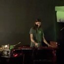 Fotografie zachycuje kapelu během hraní. V centru je červený klavír s nápisem nord electro 6, za kterým stojí osoba v zeleném tričku. Vpravo je vidět…