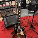 Elektrická kytara s tmavě hnědým gradientem (sunburst) a bílým pickguardem. Na hlavě je viditelné logo Epiphone. Kytara má dva humbuckery, čtyři otoč…